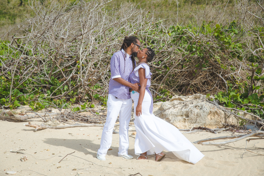 St. Croix bride and groom kissing on rocky beach with large bushes in the background